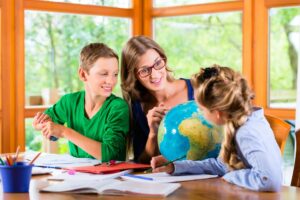 Mother sitting at a desk with her two children, pointing at a globe during a homeschool lesson