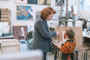 Woman helping a child paint at an easel in an art room