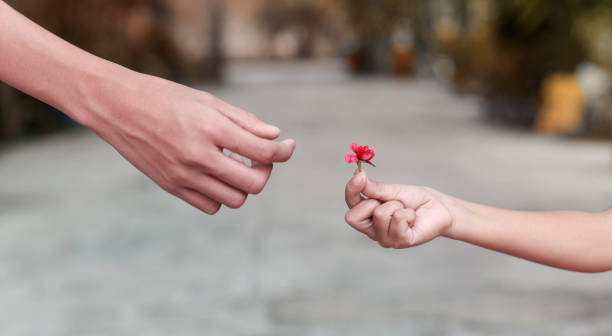 A hand reaching out to receive a small flower from another person, symbolizing kindness, generosity, and human connection.