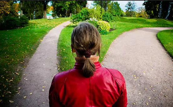 A woman stands at a fork in a park pathway, facing two different directions, symbolizing life's choices, personal growth, and intentional decision-making.